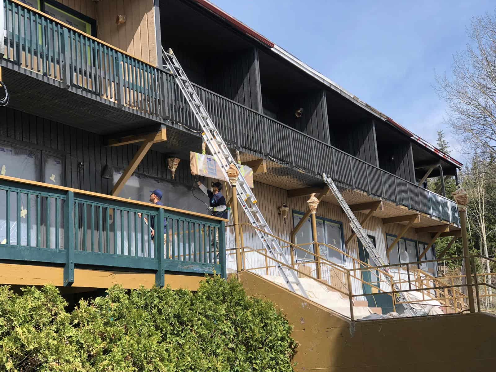 Painters working on a multi-storey building exterior with ladders and surface protection
